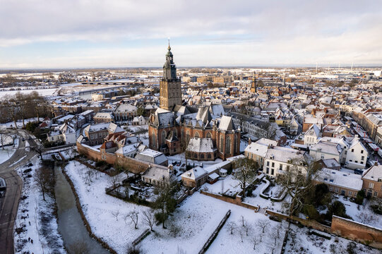 Warm sunlight on medieval Hanseatic Dutch tower town Zutphen in the Netherlands covered in snow with historic heritage buildings and river IJssel passing by in the background behind Walburgiskerk chur