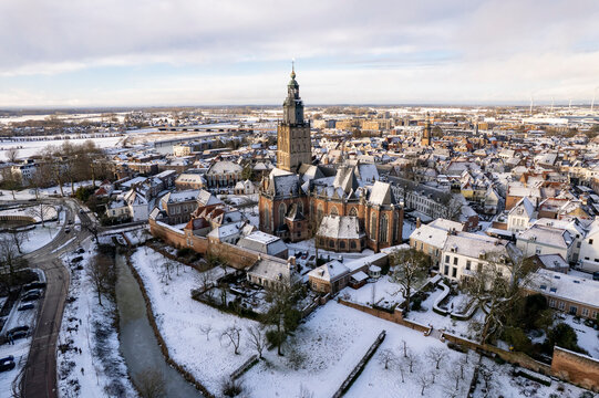Warm sunlight on medieval Hanseatic Dutch tower town Zutphen in the Netherlands covered in snow with historic heritage buildings and river IJssel passing by in the background behind Walburgiskerk chur