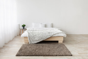Fototapeta na wymiar Home nordic interior. Minimalist design with panoramic window. King size bed on wooden floor, table with green plants in pots, carpet on white wall background in bedroom interior, empty space