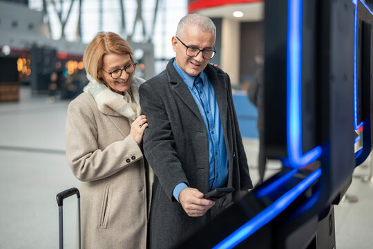 Senior couple using self-service check-in kiosk at airport - Powered by Adobe