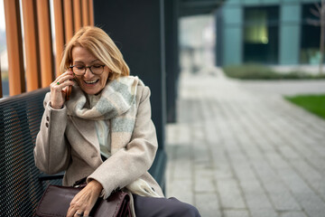 Obraz premium Mature woman laughing heartily during phone call outdoors