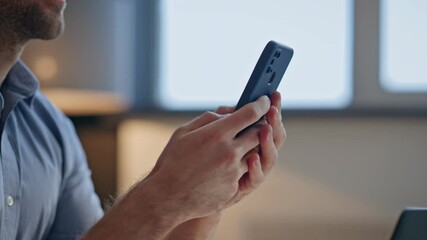 Man in blue shirt uses modern smartphone with both hands indoors - Powered by Adobe