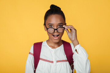 Surprised teenage african american female pupil taking off glasses and looking at camera, isolated...