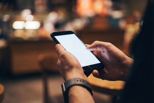 Close up of male hands holding horizontal smartphone with blank white screen in blurred cafe setting - Powered by Adobe