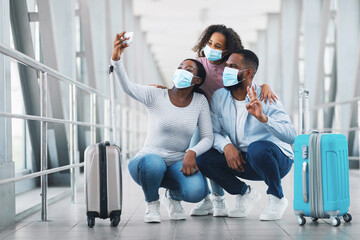 Pandemic Vacation Concept. Young Black Family In Protective Medical Masks Taking Selfie Photo With Smartphone In Airport Terminal, Travelling Together During Covid-19, Dad Showing Peace V Victory Sign
