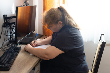 Mature woman writing notes at home office desk