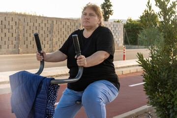 Overweight woman exercising outdoors on park equipment