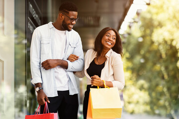 Portrait of happy black couple in love making shopping on weekend, walking down the street with colorful bags, spending time together, talking and laughing, enjoying sunny day, copy free space © Prostock-studio