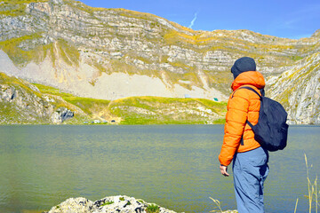 Backpacker overlooking Kapetanovo jezero surrounded by rocky peaks and green highland terrain in Montenegro. Symbolizes wilderness discovery, sustainable tourism values, and remote destination appeal.