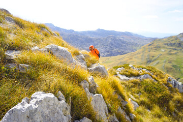 A landscape with yellow grass, scenic mountain slopes, and a hacker walking along a trail. Illustrates ecotourism in Montenegro, slow adventure philosophy, outdoor exploration, and wanderlust concept.