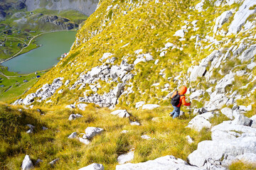Backpacker descending rocky hillside with alpine lake visible below in Montenegro wilderness. Illustrates off grid travel appeal, independence mindset, and tourism away from crowded destinations.