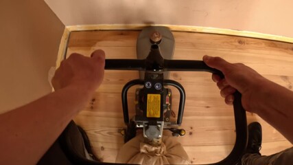 POV of a contractor guiding a floor sander across wooden planks, moving forward to smooth the surface during a detailed renovation pass.