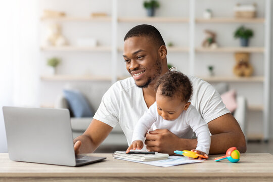 Young Black Man Study With Laptop At Home And Taking Care About Baby, African American Father Using PC Computer For Online Education While Babysitting His Adorable Infant Child, Copy Space
