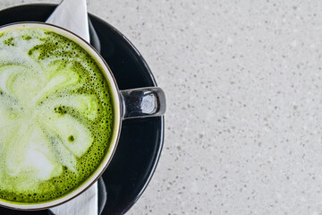 Top view of a half hot matcha latte in the black mug or cup. flat lay. high angle, above. tissue. table. grey or gray. white. green. copy space, empty, free, negative, text, design. background.