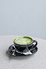 Close up view of hot matcha latte in the black mug or cup. spoon. stainless steel. tissue. table. grey or gray. white. green. copy space, empty, free, negative, text, design. Side. front. vertical. ss