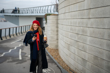 Woman smiling checking phone walking outdoors with coffee