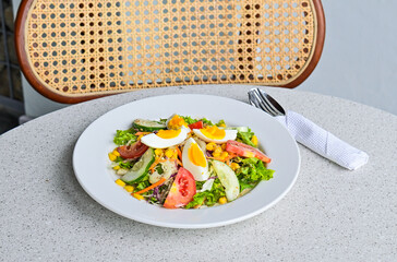 close up view of egg salad on the white plate. cruttong. mix salad. boiled egg. dressing. vegetables. high angle, above. granite table on the background. spoon, fork and tissue. stainless steel. grey.