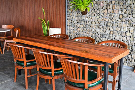 Empty long wooden table And chairs. grey or gray rocks on the wall. outdoor seating for restaurant, Cafe or coffee shop. Plants, leaves, green, nature, wall. wood. brown. trellis. hanging, hang. decor