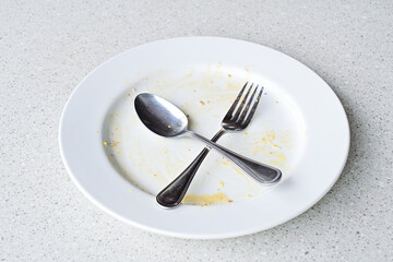 Empty plate with leftover food and utensils after a meal. close up view. isolated. granite table on the background. fork and spoon. stainless steel. crossed, cross. x. leftovers. eat, eating, ate. 