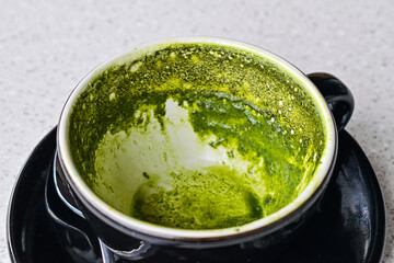 Photo of empty hot matcha latte cup after drinking. Black cup or mug with spoon. Glass table. Cafe, coffe shop. Close up view. tissue. close up view. leftover. 