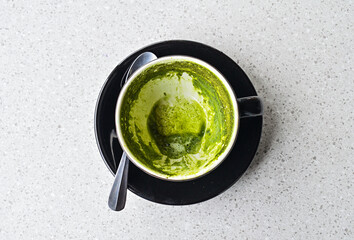 Photo of empty hot matcha latte cup after drinking. Black cup or mug with spoon. Glass table. Cafe, coffe shop. Close up view. tissue. close up view. leftover. Top, high angle, above, flat lay.