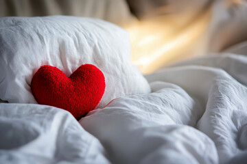 Red fabric heart resting on soft white bed sheets, creating a romantic scene for love, valentine's day, anniversaries, and special intimate moments.