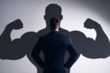A confident businessman in a suit stands tall, his shadow revealing a muscular physique, symbolizing inner strength and ambition in a competitive corporate world.