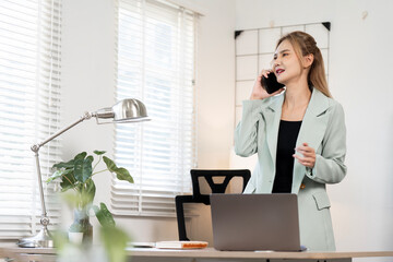 Confident Asian businesswoman in a light green blazer talking on a smartphone while standing at a...