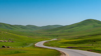 Winding Asphalt Road Passing Through Lush Green Rolling Hills Under Blue Sky 