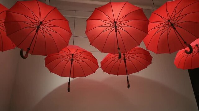 Red umbrellas suspended from the ceiling in a modern, indoor setting viewed from below