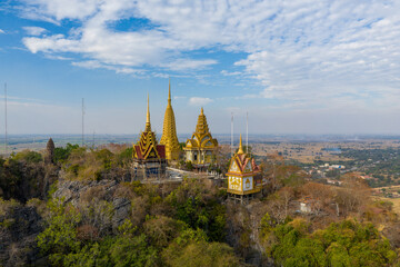 Cluster of ornate golden and red-roofed pagodas perched on the rocky summit of Phnom Sampov, overlooking a vast rural landscape near Battambang, Cambodia. The scene features intricate temple spires