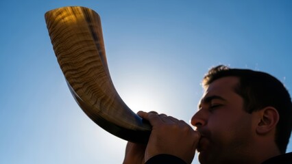 Man blowing shofar during a religious ceremony. Jewish holiday of Rosh Hashanah or Yom Kippur. Traditional sound against a bright blue sky.