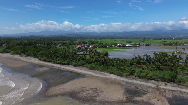 Scenic aerial drone footage of Roxas in Oriental Mindoro, Philippines showing sandy beaches, green rice fields and mountains in the background, perfect tropical landscape view.
