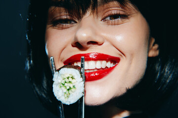 Smiling woman with red lips holding sushi, showcasing a vibrant and joyful sushi experience in a modern setting.