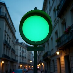A green traffic light stands tall on a city street at dusk with buildings in the background