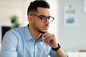 Portrait of serious young Arab businessman in formal wear and glasses thinking over problem,...