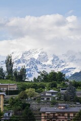 Scenic alpine landscape in Aosta Valley, Italy. Mountain village in a green valley surrounded by high peaks with snow and clouds, showing natural beauty and rural life.