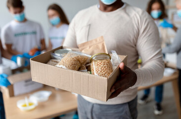 A senior black man holds a donation box filled with various food items such as grains, canned...