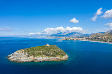 Rocky Isola di Cirella covered in green vegetation sits in clear blue Mediterranean waters, with a historic stone tower and sweeping views of the Calabrian coast and distant mountains under a bright