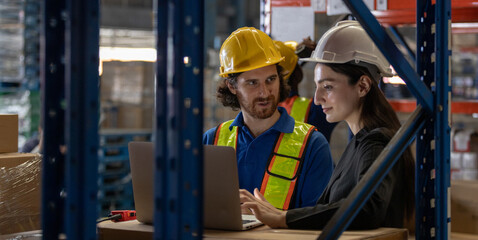 Warehouse manager and logistics worker collaborating on laptop in storage area, representing teamwork, digital planning, modern supply chain operations in industrial logistics.