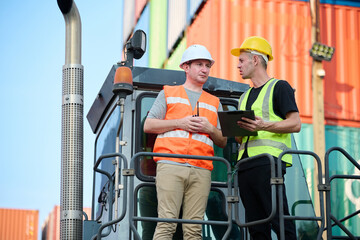 Workers discussing their project plan in containers yard. They are wearing hard hats and safety vests
