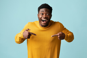 Laughing attractive young black guy pointing at his yellow sweater, happy african american...