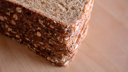 A stack of multigrain bread slices with seeds and oats on the crust sits on a wooden surface showing detailed texture and wholesome ingredients in natural light
