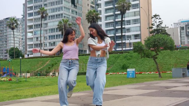 Two cheerful young women dancing together in a city park