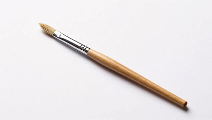 Fototapeta premium A single artist's paintbrush featuring a natural wooden handle and a silver ferrule rests diagonally on a clean white background, showcasing its fine, pointed bristles and minimalist aesthetic.