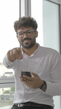 Confident young businessman pointing at camera while using phone