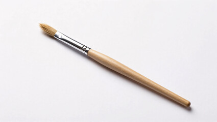 Naklejka premium A single artist's paintbrush featuring a natural wooden handle and a silver ferrule rests diagonally on a clean white background, showcasing its fine, pointed bristles and minimalist aesthetic.