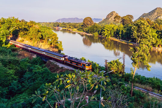 Train Journey along River Kwai. Scenic view of train traversing famous historic curve of Railway line surrounded by green hills at Tham Khao Pun Temple viewpoint. World War II Heritage Rail, Thailand.