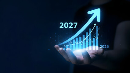 A hand holding a glowing blue bar chart showing growth from 2026 to 2027, symbolizing future business success and financial progress.
