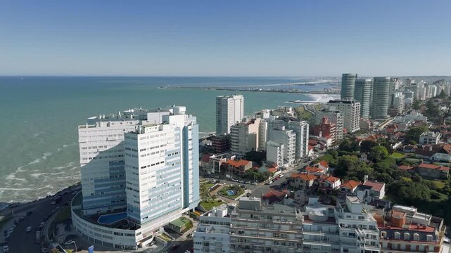 Aerial view of Cabo Corrientes and surrounding buildings in Mar del Plata, Argentina, showing Playa Grande beach and the port area in the background. The camera performs a push in movement and a crane